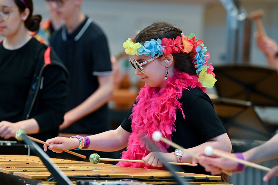 A young girl plays a drum and smiles