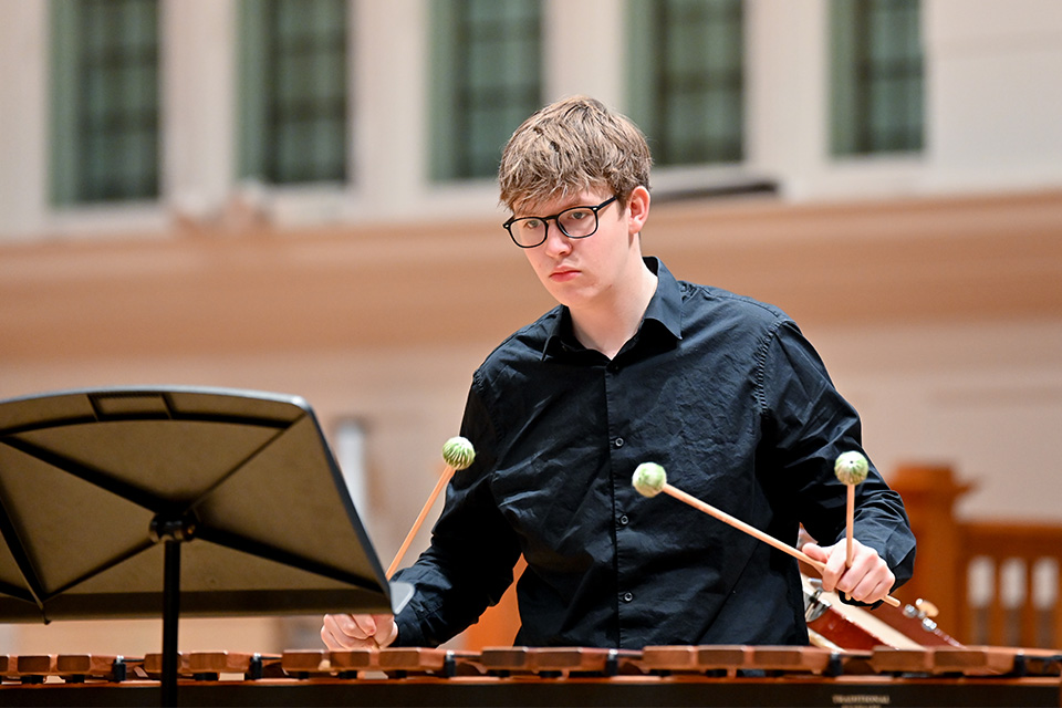 A young man plays the marimba with four mallets on stage