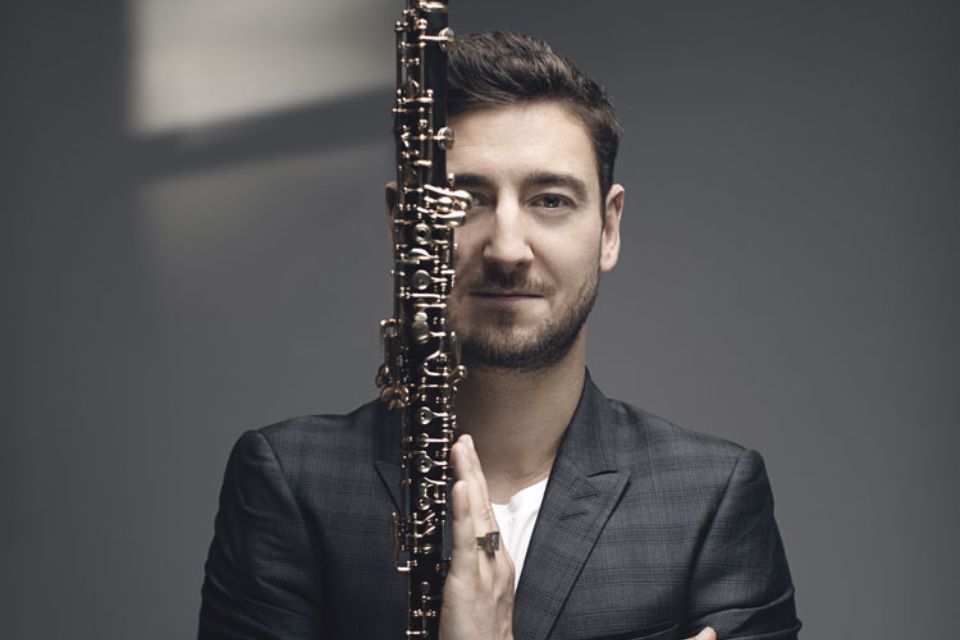 Philippe Tondre wears a grey blazer and holds his oboe in front of his face