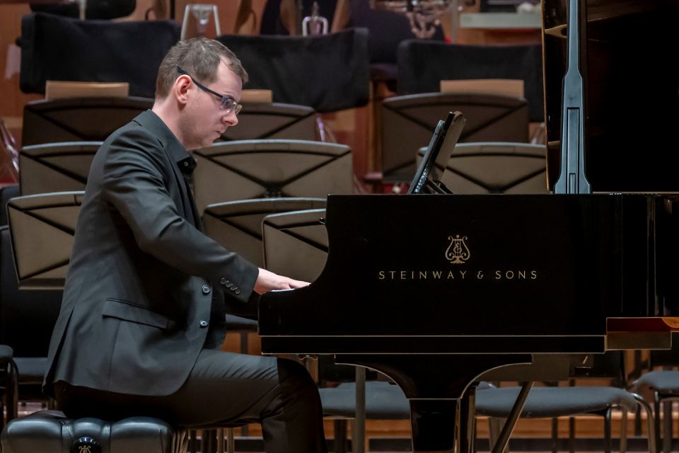 A pianist wears a black suit and performs on stage