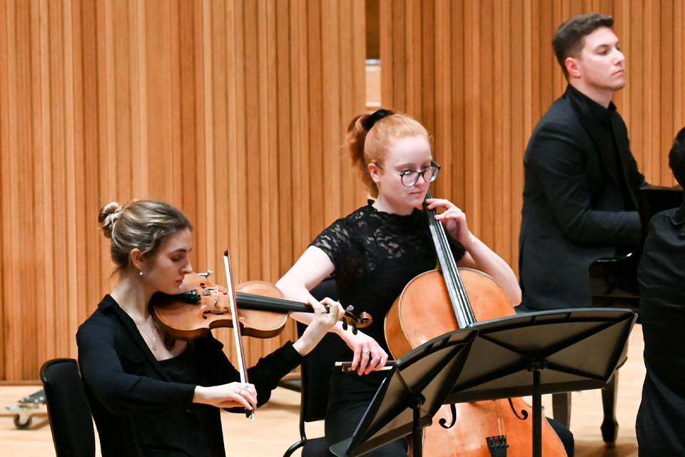 A violinist, cellist and pianist perform in a chamber group on a brightly lit stage