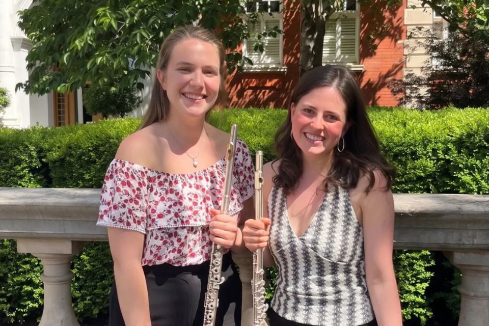 Two young woman stand outside smiling and holding flutes