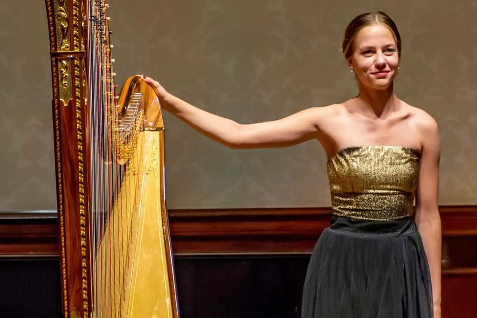 Liza Rakovska stands on stage with her harp, smiling