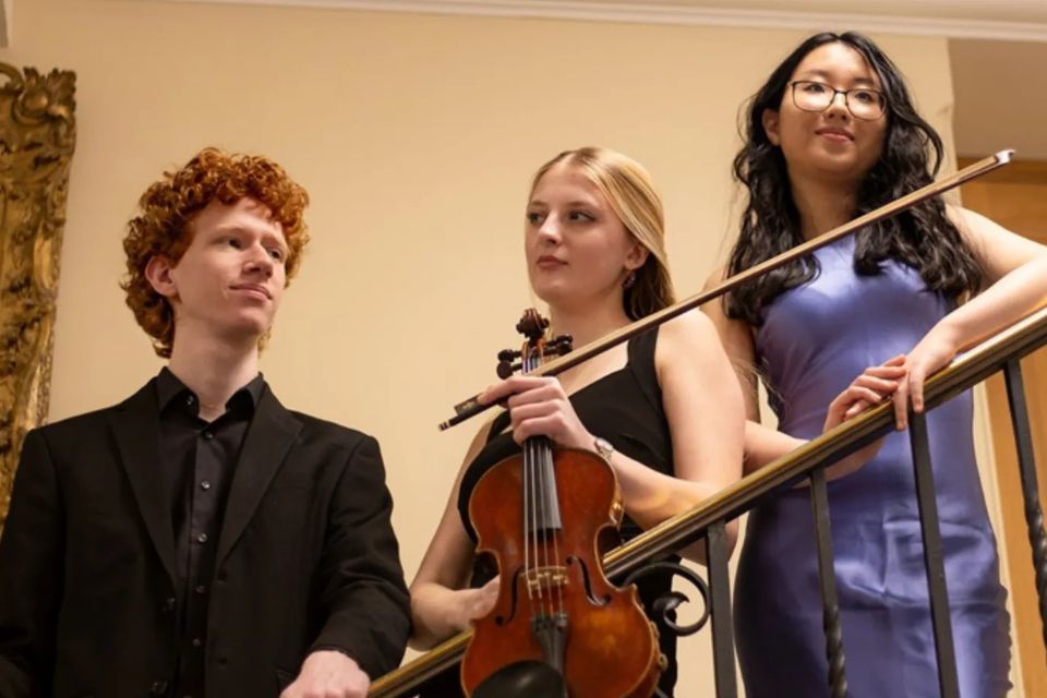 Two women and a man stand on a staircase holding a violin and cello