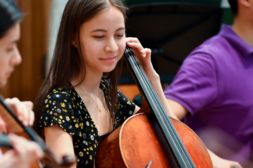 A girl from the Junior Department plays the cello, smiling