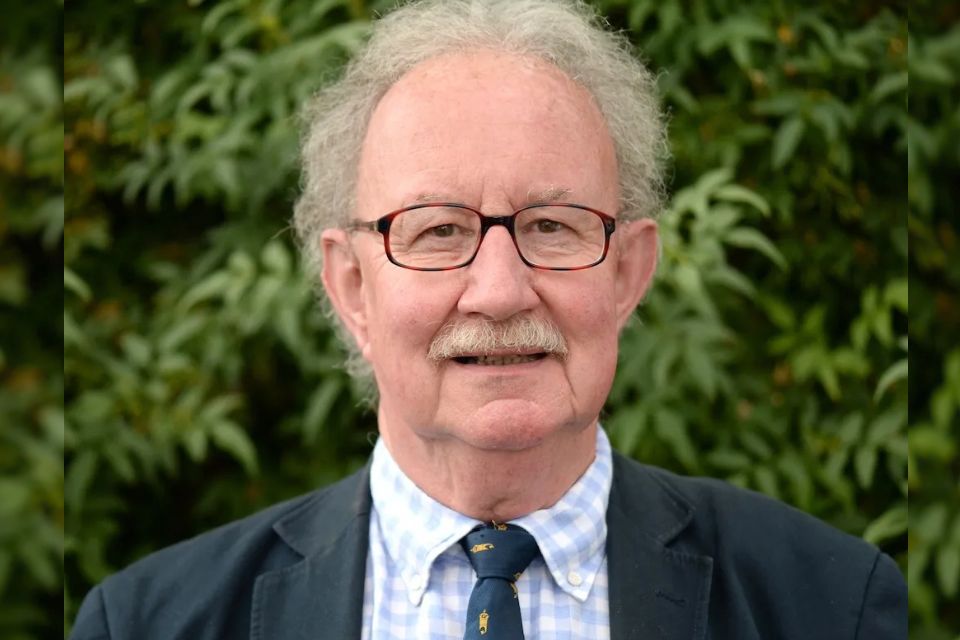 Richard Langham Smith wears a suit and tie and glasses and stands outside smiling