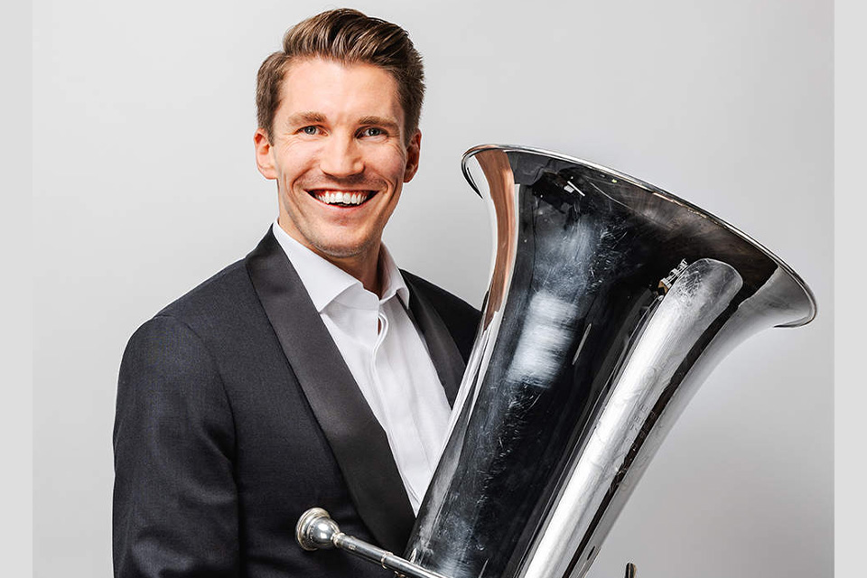 Ross Knight wears a white shirt and holds his tuba, smiling broadly