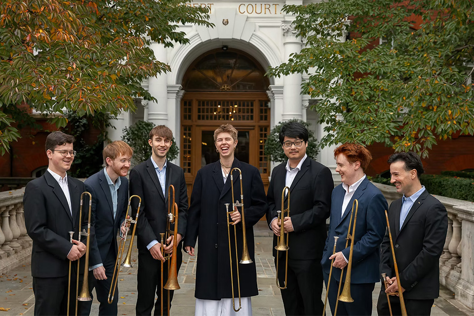 A group of musicians holding sackbuts stand outside and laugh