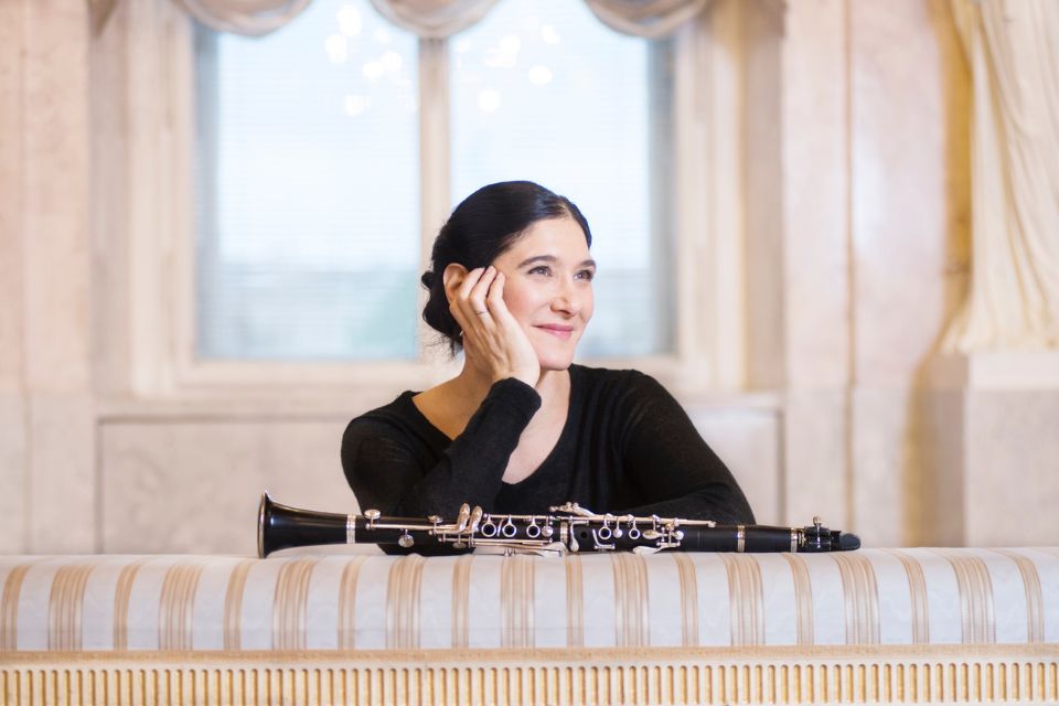 Sharon Kam rest her head on her hands next to her clarinet in a brightly lit room
