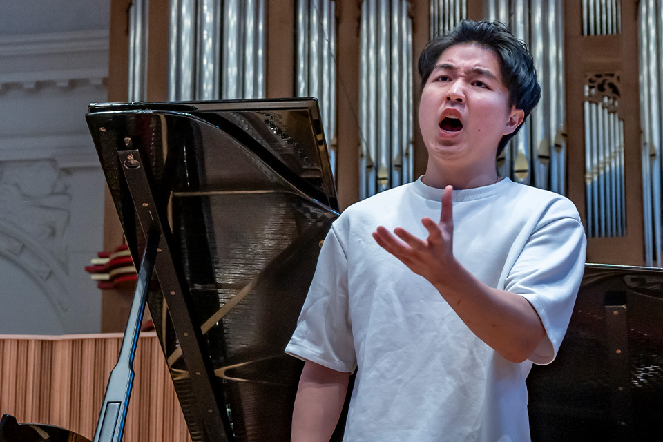 A young man wears a white t-shirt and sings passionately on stage