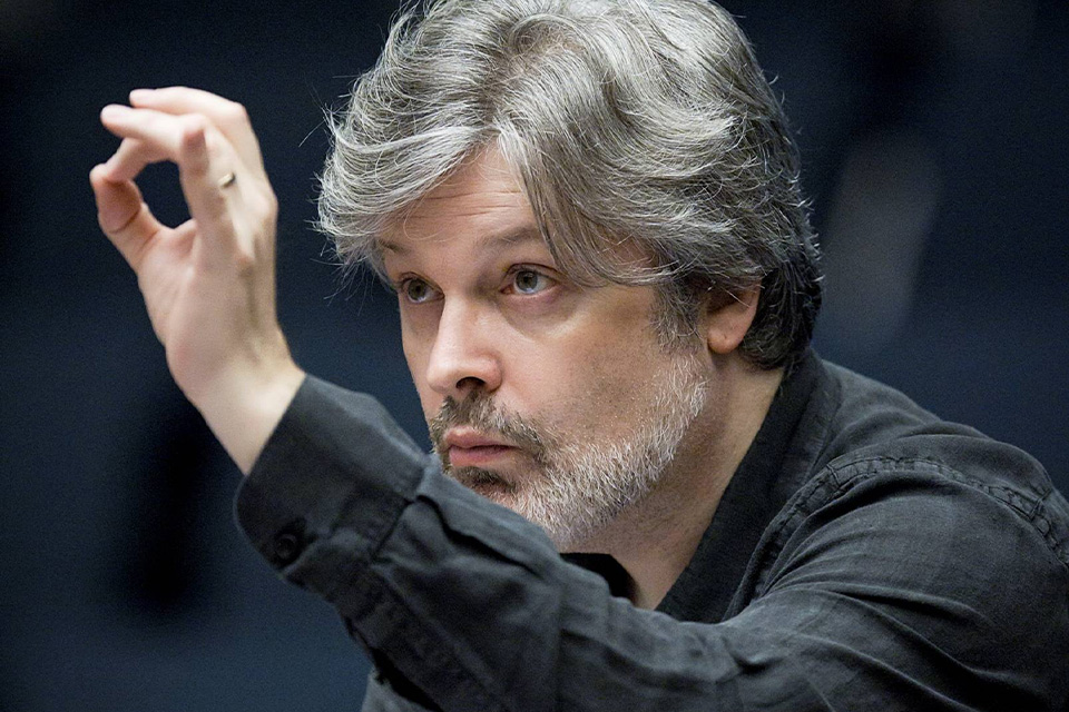Sir James Macmillian wears a black shirt and conducts with his thumb and finger together