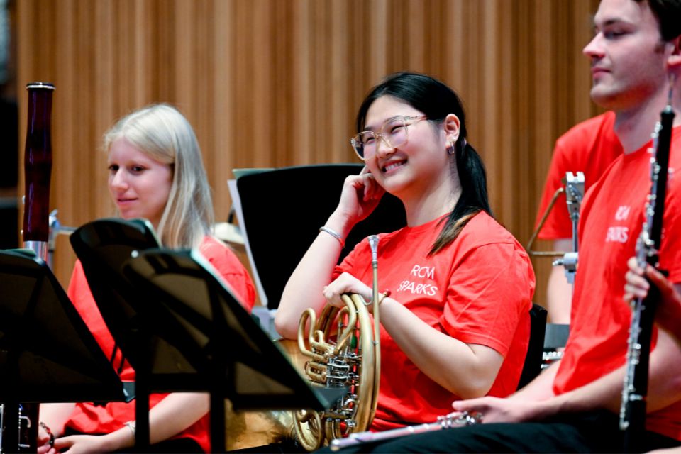 A horn player wearing a red t-shirt holds her instrument and laughs