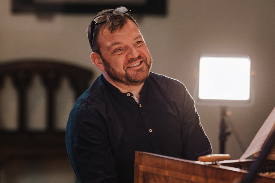 Steven Devine sits at the clavichord and smiles broadly