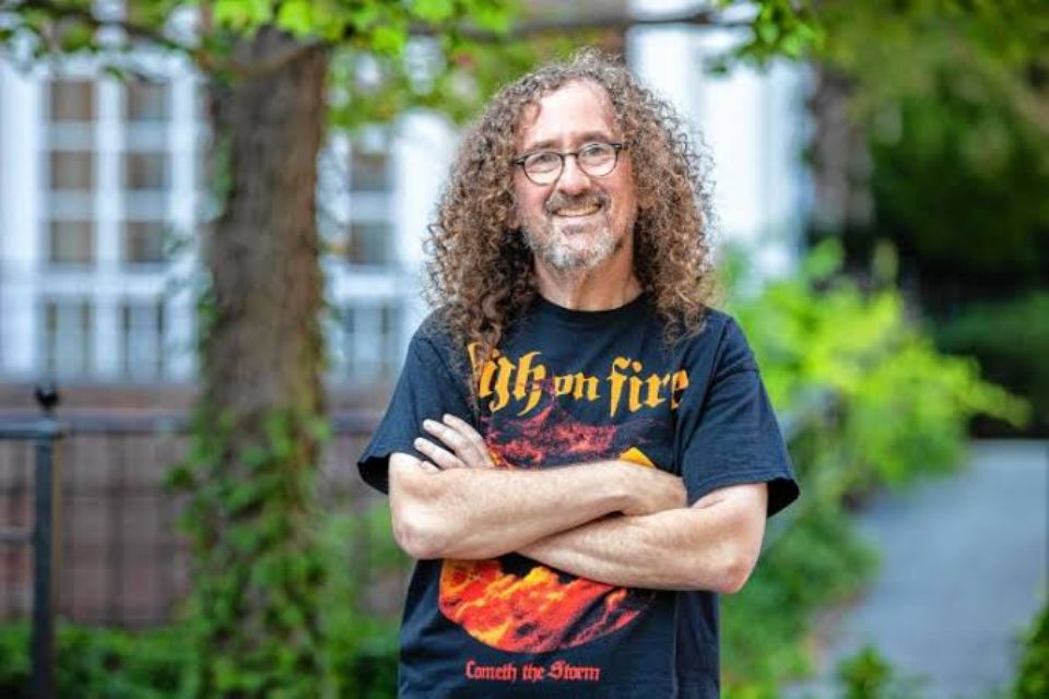 Steve Waksman stands outside in a black graphic t-shirt and smiles