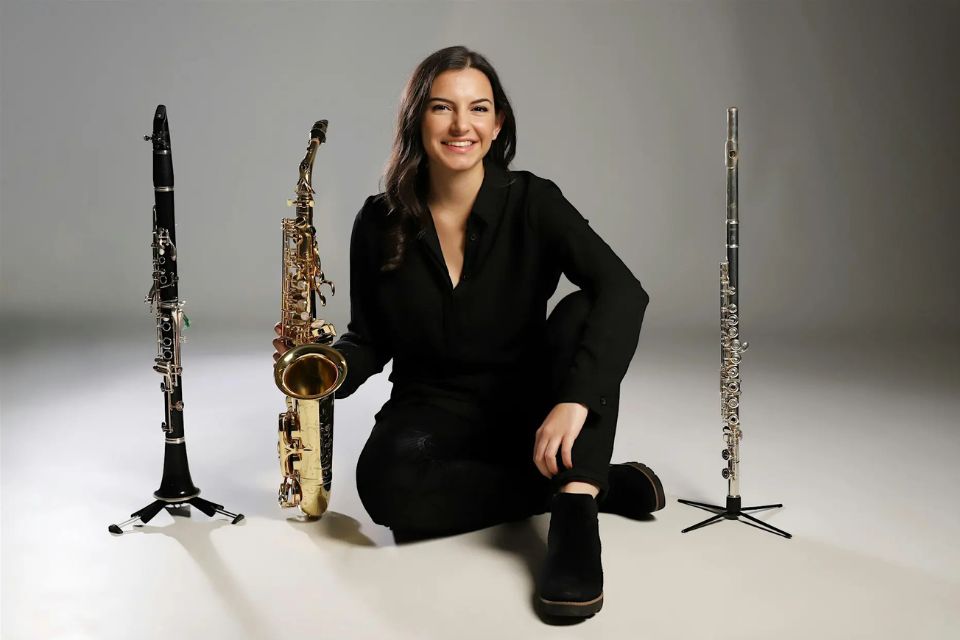 A young woman sits holding a saxophone next to a clarinet and flute