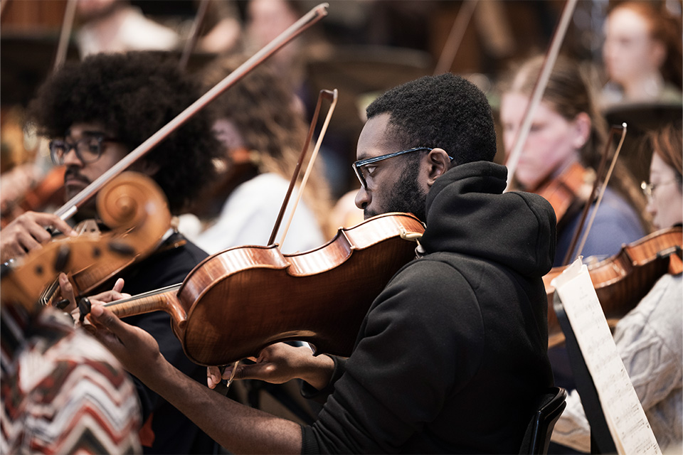 A young man plays the violin in an orchestra