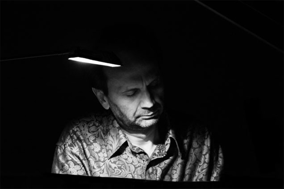 Svetozar Ivanov looks down at the piano as he plays in a dark room