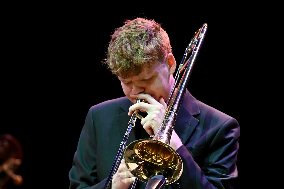 A young man plays the trombone in a dark room