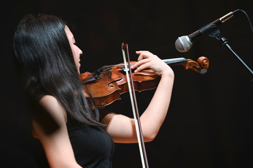 A violinst plays passionately on stage in front of a microphone