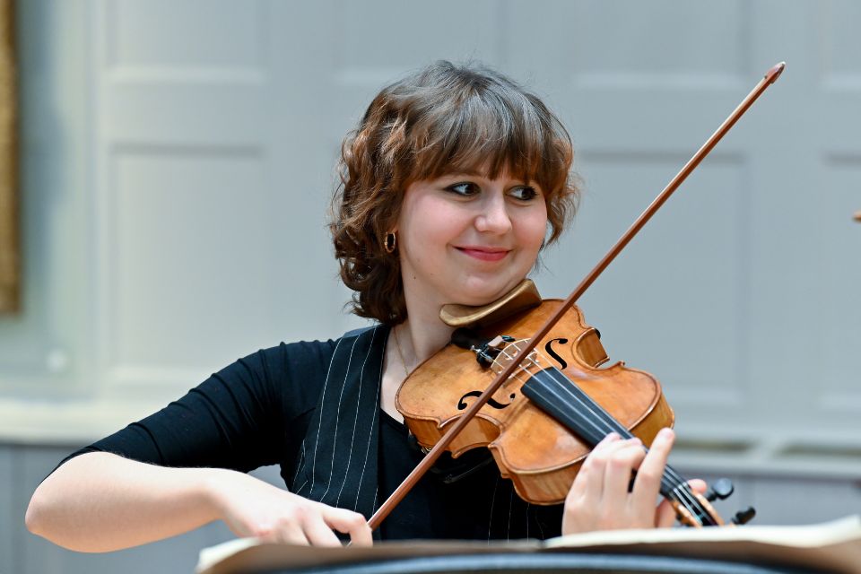 A young woman smiles as she plays the violin on stage