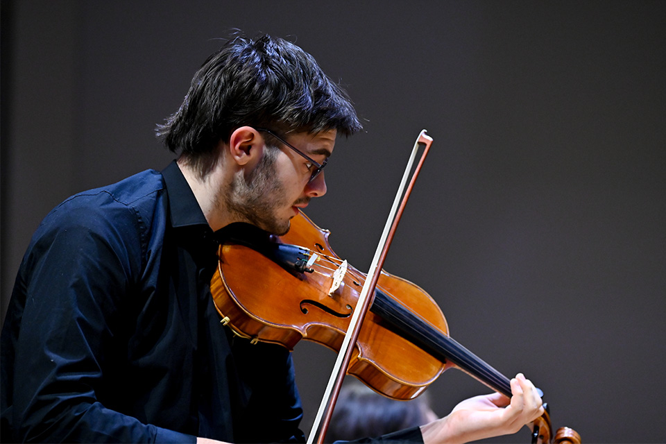 A young man wearing a black shirt and glasses plays the violin