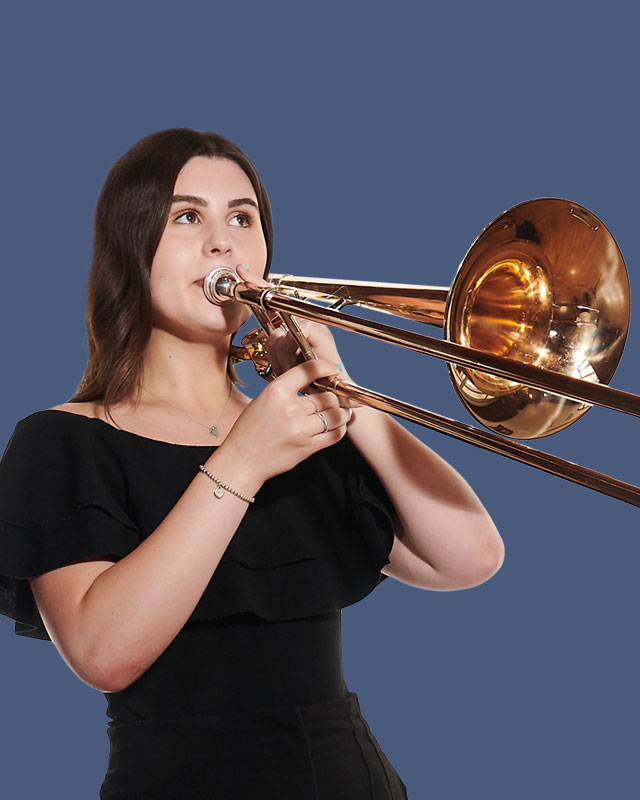A female student, wearing a black dress, playing a trombone, with a indigo background.