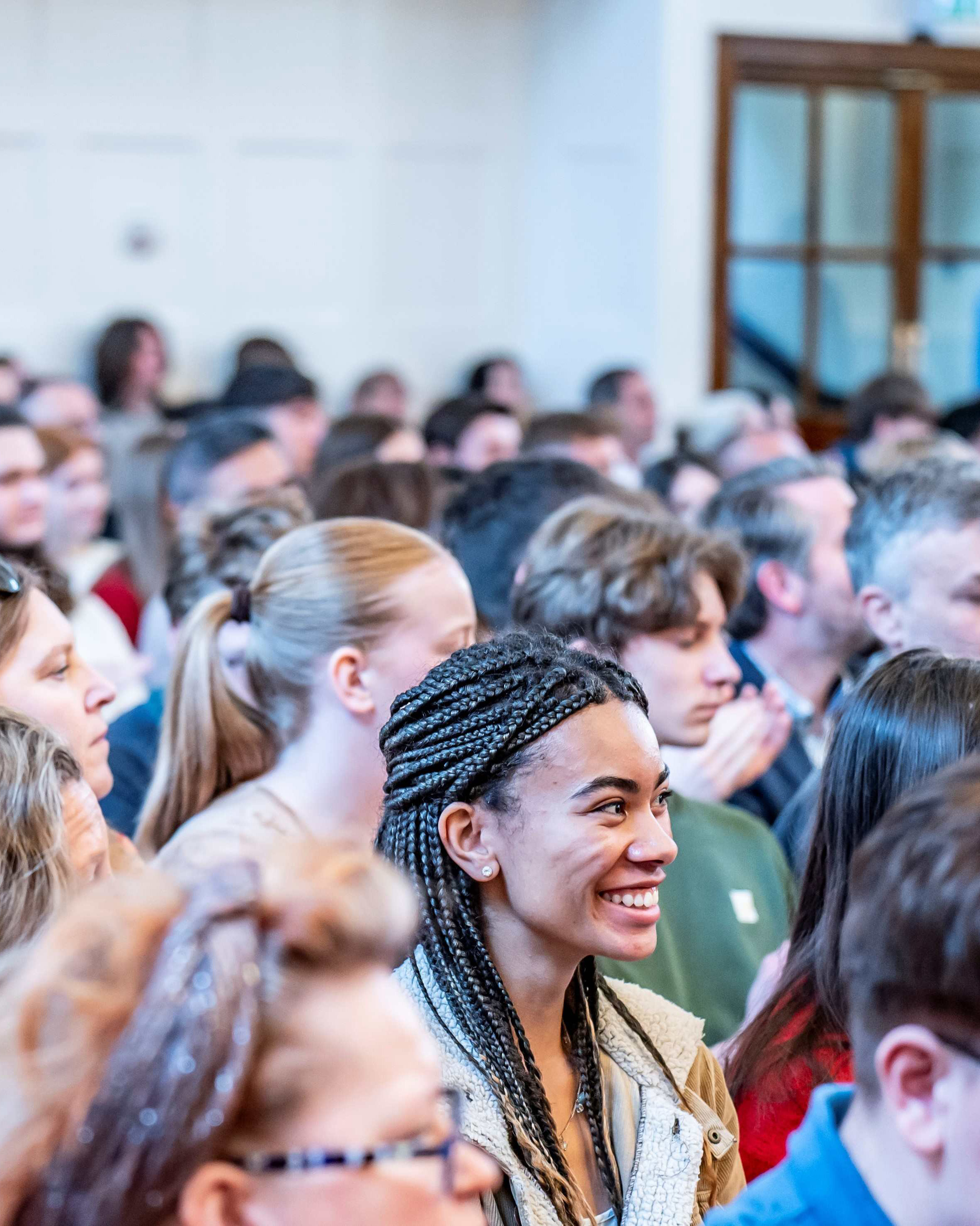 A large audience seated closely together in a bright event hall, smiling.