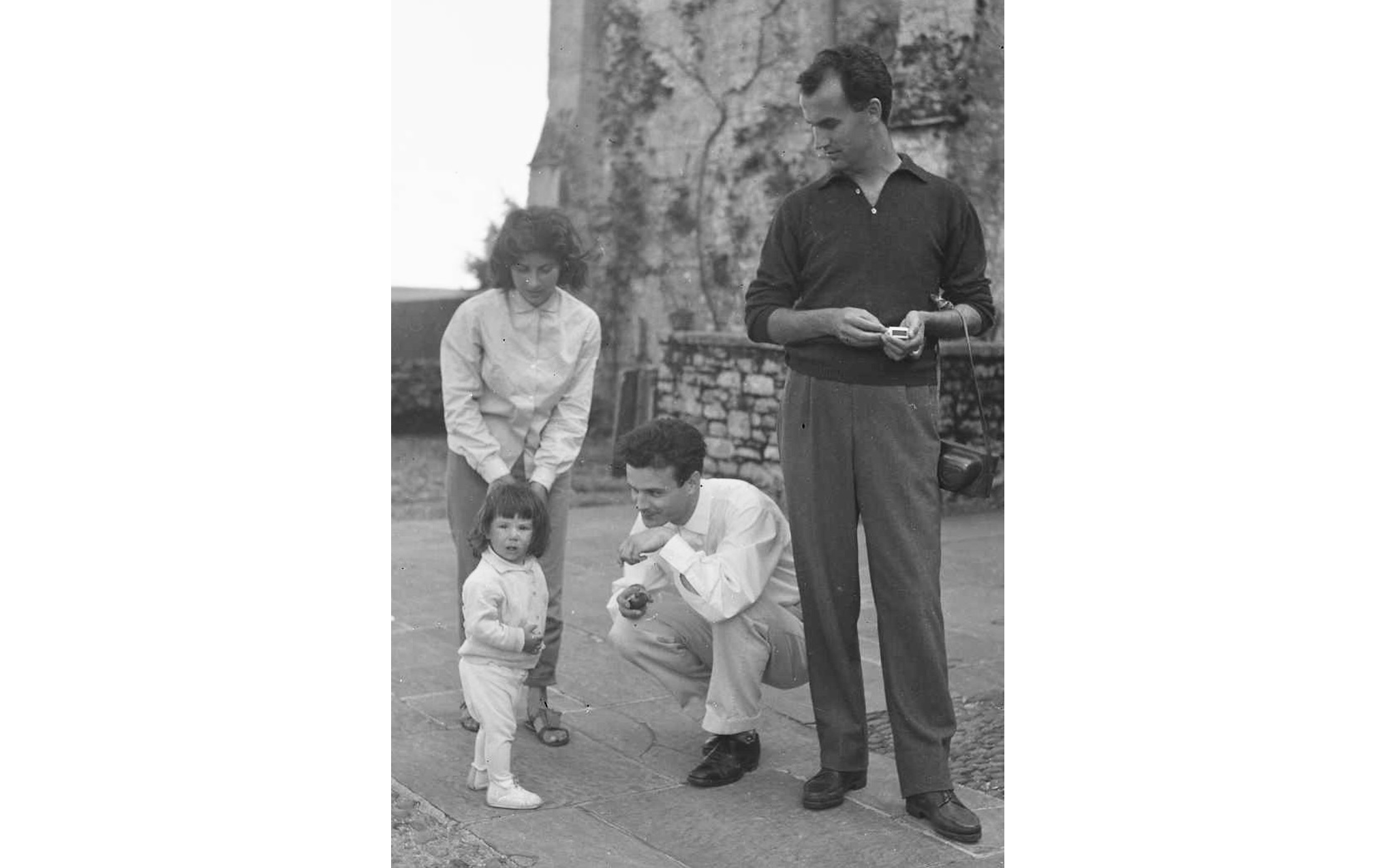 A black and white photo of two men, a women and a young girl, with the man and women interacting with the young girl.