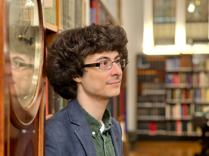 A man with wavy hair and glasses in a library